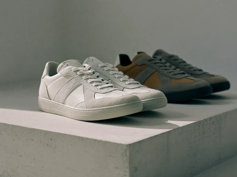 Zwei Sneaker-Paare auf einer hellen Betonstufe im weichen Seitenlicht