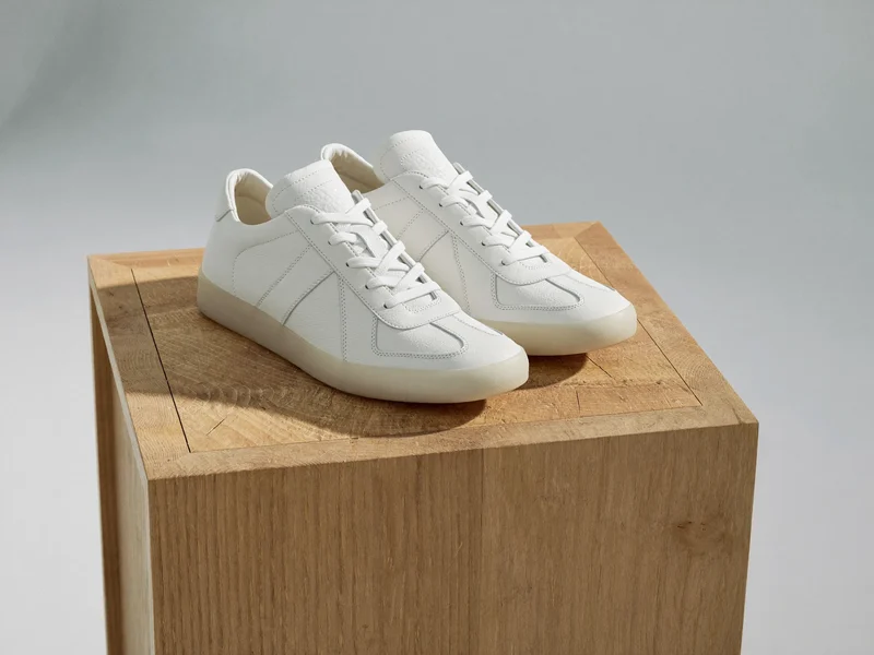 Weisse Leder-Lowtops auf einem Sockel aus heller Eiche